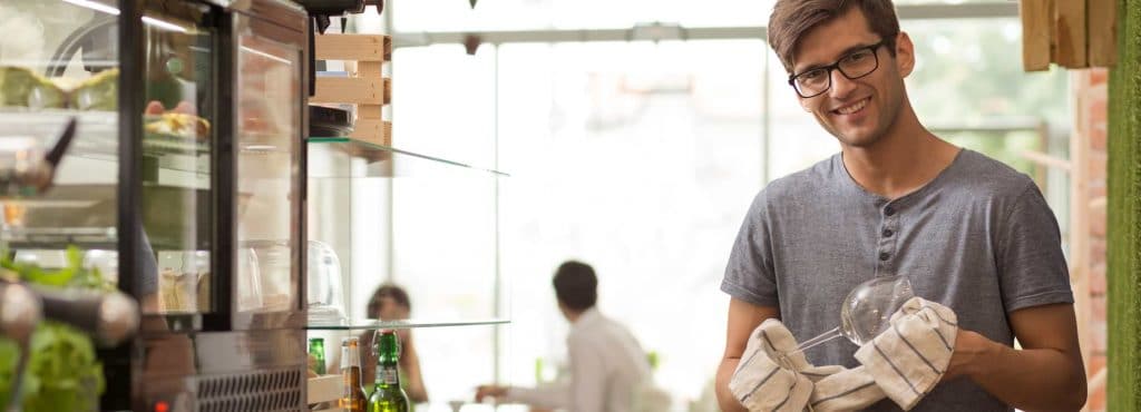 Leende man som putsar ett glas i sin restaurang